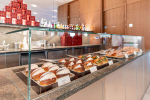 A close up of a glass display case at Bar Giorgio, showing trays of Italian pastries filled with cream, along with savoury rolls, all neatly arranged on a polished countertop, with bottles and stacked red tins in the background.